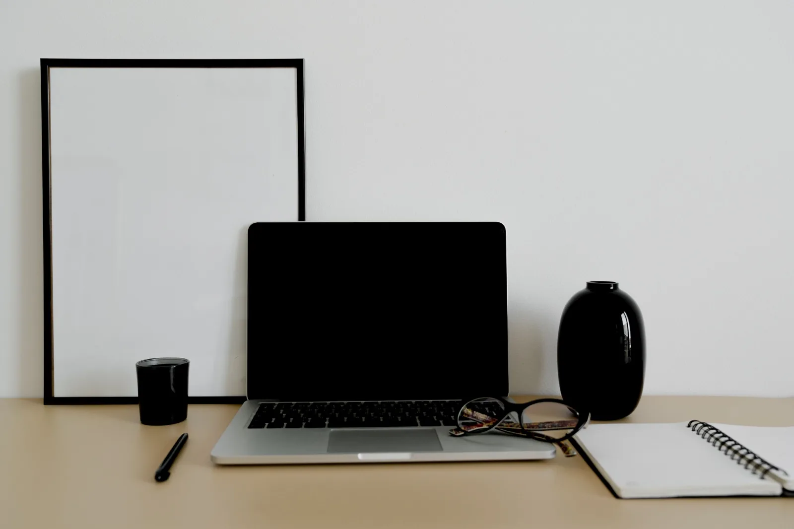 Laptop, glasses and notebook arranged on a tidy desk.