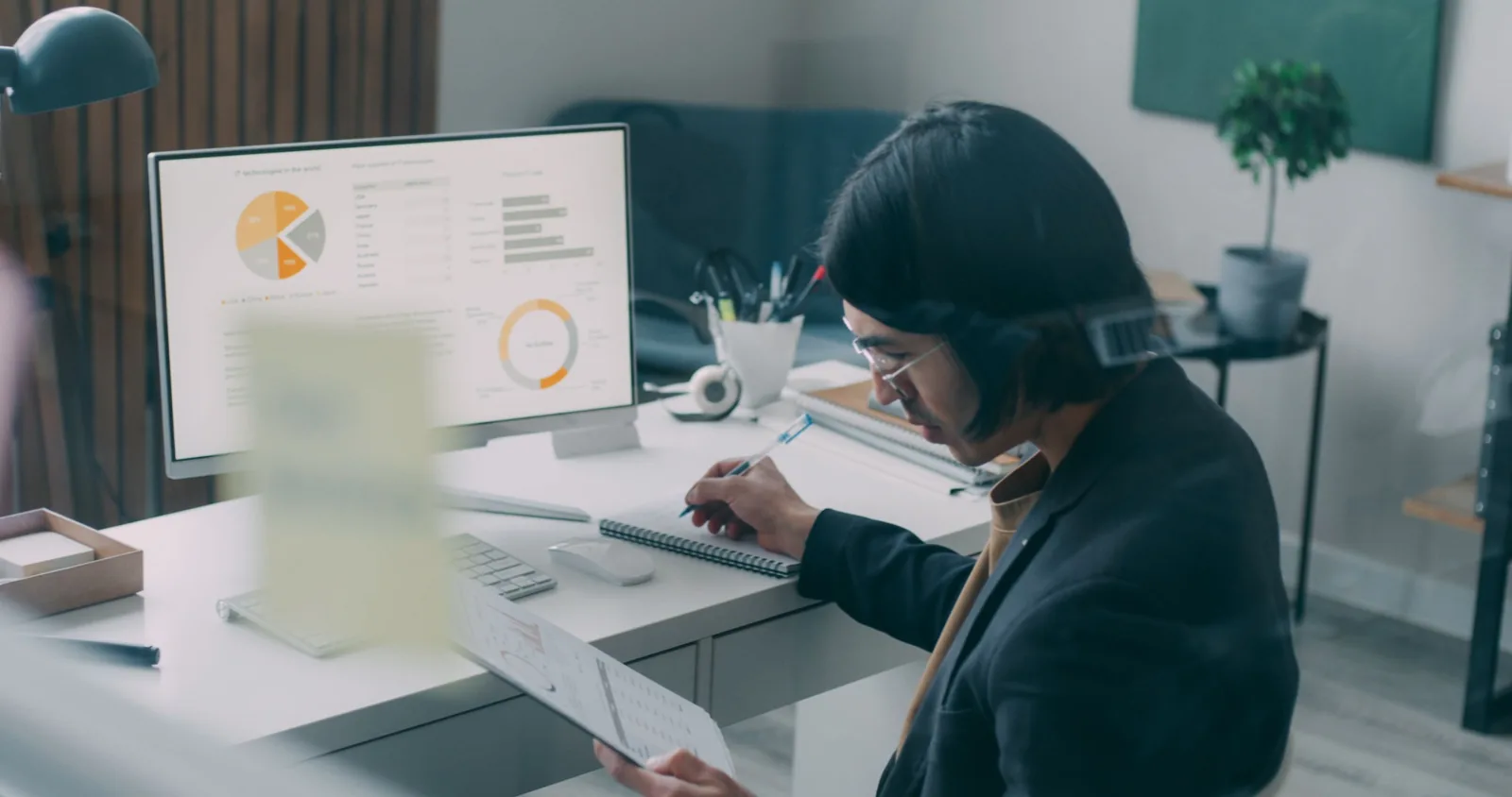 Professional reviewing charts on a desktop monitor and taking notes.